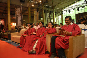 Individuals in red academic gowns seated in a well-lit venue during a convocation ceremony.