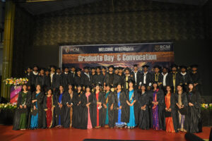Graduates in caps and gowns at RCM Global School convocation ceremony with floral decorations.
