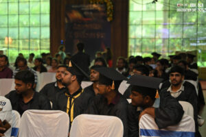 Graduates in black gowns and caps seated indoors for BBA and BCA graduation ceremony 2025.