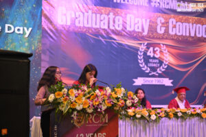 Graduation ceremony with speakers at decorated podium, featuring "Graduate Day & Convocation" banner.