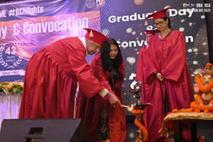 People in red gowns lighting a lamp at a "Graduation Day & Convocation" event with Ganesh idol.
