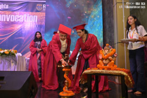 Graduation ceremony with red gowns, lamp lighting, Ganesha idol, and a "Convocation" banner.