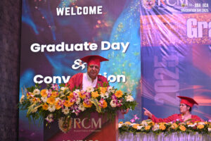 Man delivers speech at podium adorned with flowers during RCM Graduate Day & Convocation.