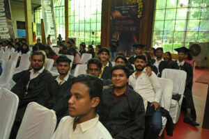 Graduation ceremony with attendees in gowns and caps in a decorated indoor hall.