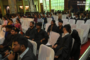 Graduation ceremony attendees in caps and gowns, banners read "Graduation Day 2K25."