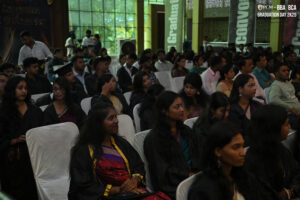 Graduation ceremony with BBA and BCA students in gowns, seated indoors, formal setting.