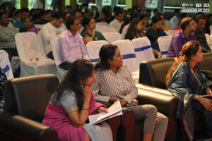 People seated in a hall with white chairs during a BBA/BCA graduation event, 2025 banner visible.