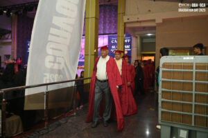 Individuals in red graduation robes walking in an indoor ceremony procession.