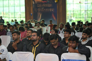 Individuals in black gowns seated at a formal event with white chairs in the background.