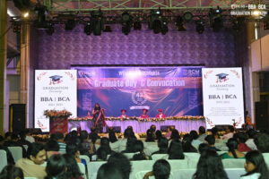 Graduation ceremony for BBA and BCA 2022-2025 with stage and audience in a decorated hall.