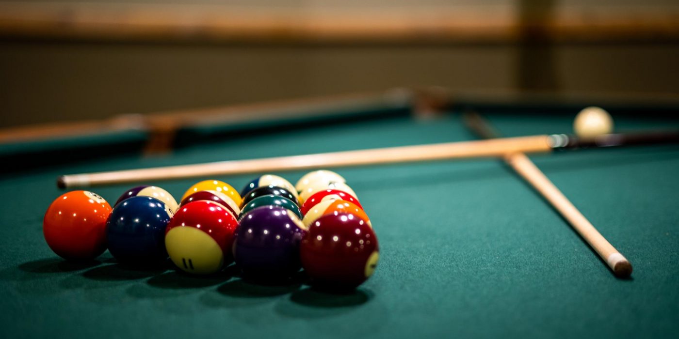 Pool Table Setup Pool balls in a triangle on a green table with cues nearby and cue ball in background.
