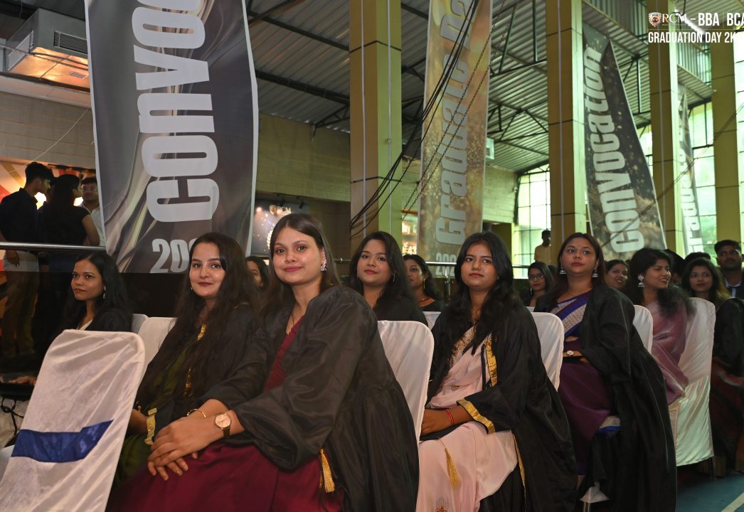 Individuals in academic gowns seated at a 2023 convocation event with celebratory banners.